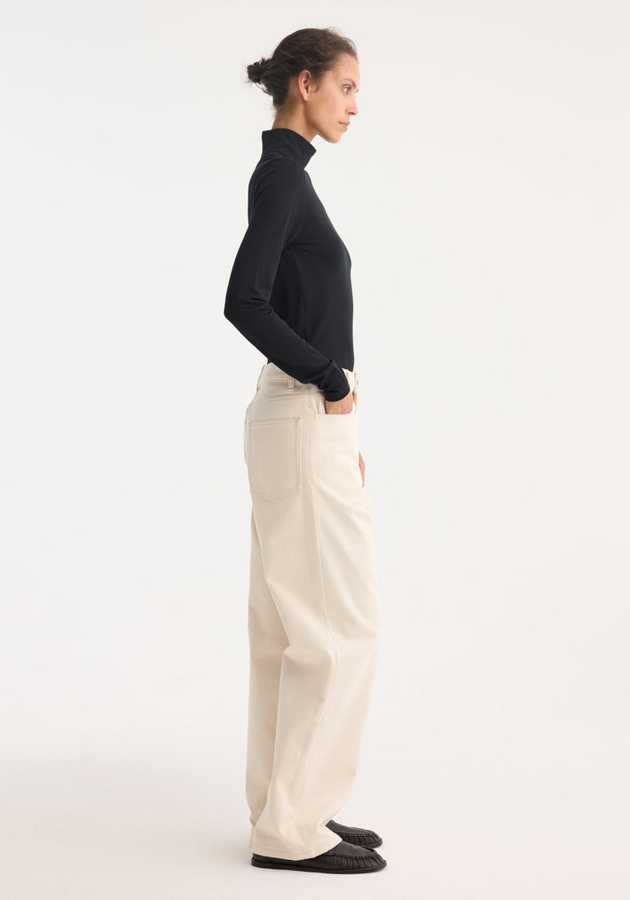 Woman in profile wearing Fine merino turtleneck | black, fitted silhouette with long sleeves, paired with high-waisted trousers. Hand tucked into pocket.