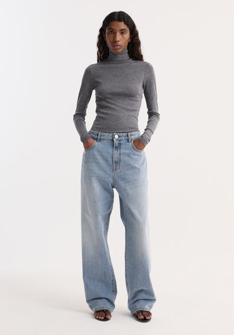 Model wears Fine merino turtleneck | mid grey melange, showcasing a fitted silhouette with long sleeves, paired with high-waisted jeans and dark sandals.