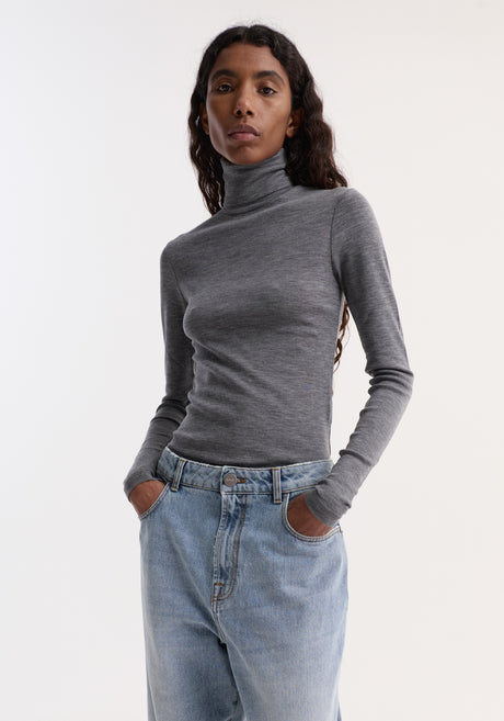 Model wears Fine merino turtleneck | mid grey melange, showcasing a fitted silhouette with long sleeves, paired with high-waisted jeans and dark sandals.