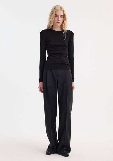 Model wears Fine merino long sleeve in black, a crew neck, form-fitting top crafted from 100% merino wool, tucked into high-waisted, wide-leg trousers.