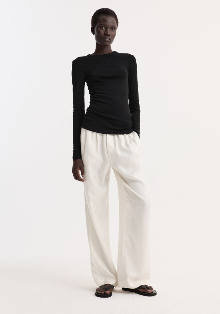 Model wearing Fine merino long sleeve in fitted silhouette, paired with high-waisted trousers and sandals, highlighting minimalist style.