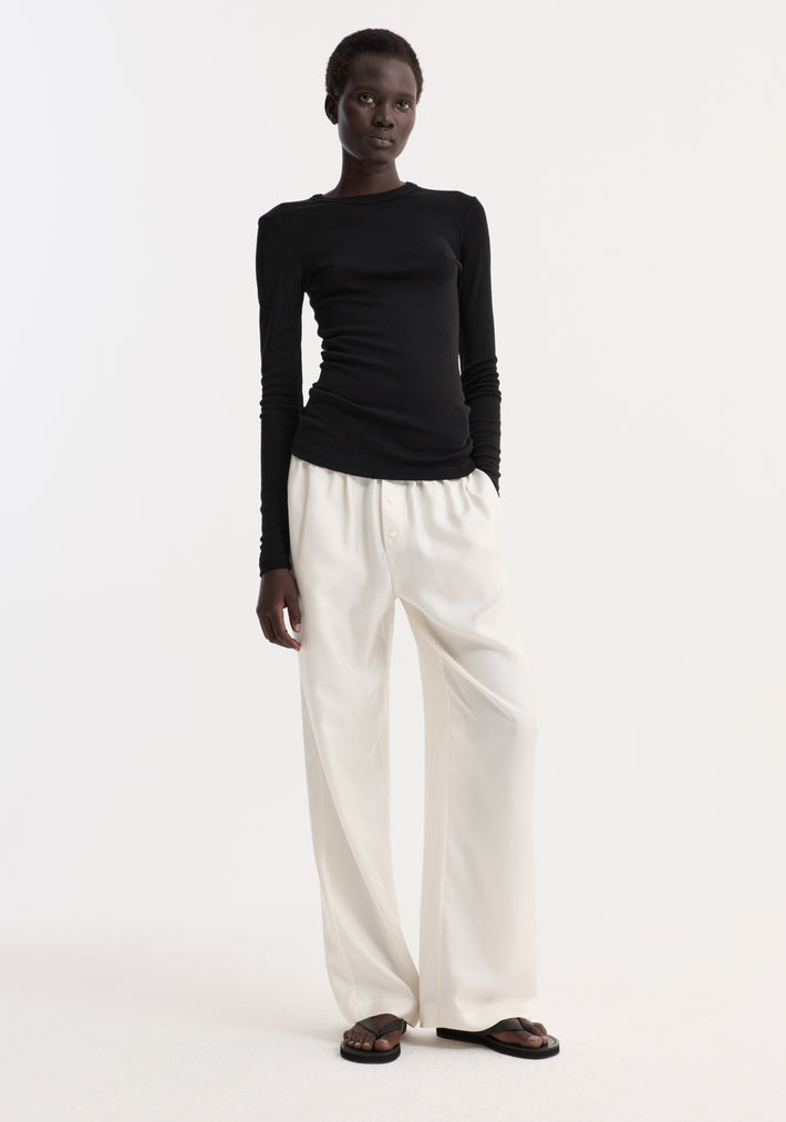 Model wearing Fine merino long sleeve in fitted silhouette, paired with high-waisted trousers and sandals, highlighting minimalist style.
