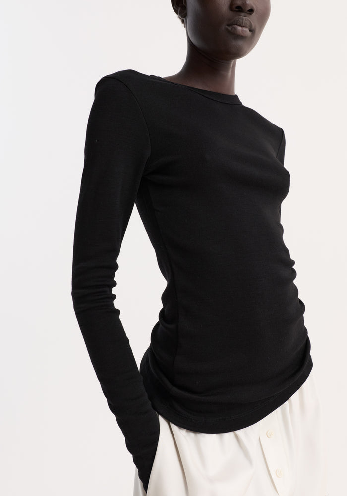 Model wearing the Fine merino long sleeve in black, showcasing its fitted silhouette and crew neck, paired with a loose, white bottom garment.