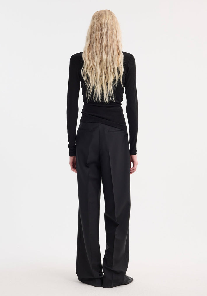 Model with back turned showcases Fine merino long sleeve | black, featuring a fitted silhouette and crew neck, paired with wide-leg trousers.
