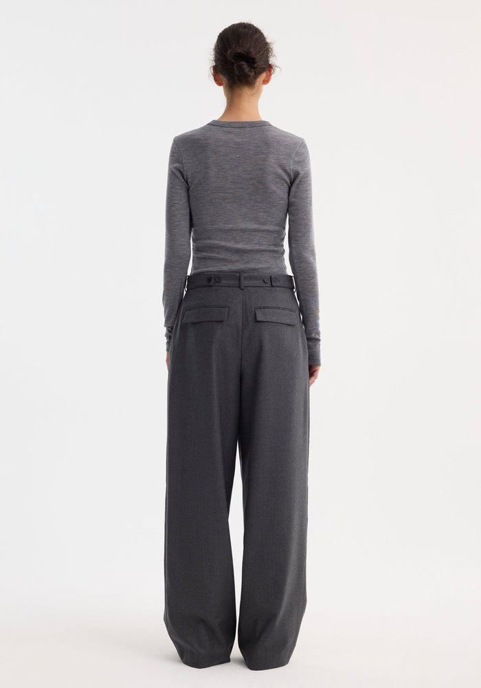 Back view of a person wearing a fitted Fine merino long sleeve in mid grey melange, tucked into high-waisted wide-leg trousers, hair styled in a bun.