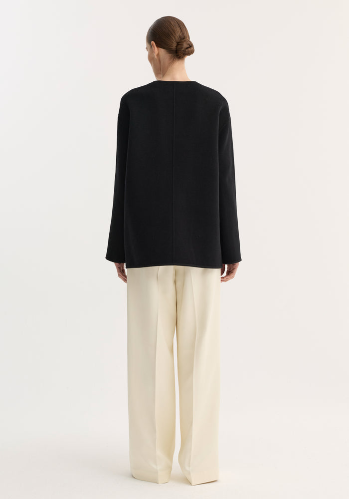 Model in rear-view wearing loose black top and cream trousers, showcasing the Mandarin double-faced wool jacket with pankou closure and embroidered edges.