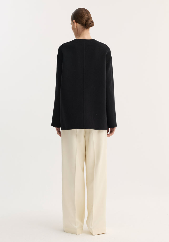 Model in rear-view wearing loose black top and cream trousers, showcasing the Mandarin double-faced wool jacket with pankou closure and embroidered edges.