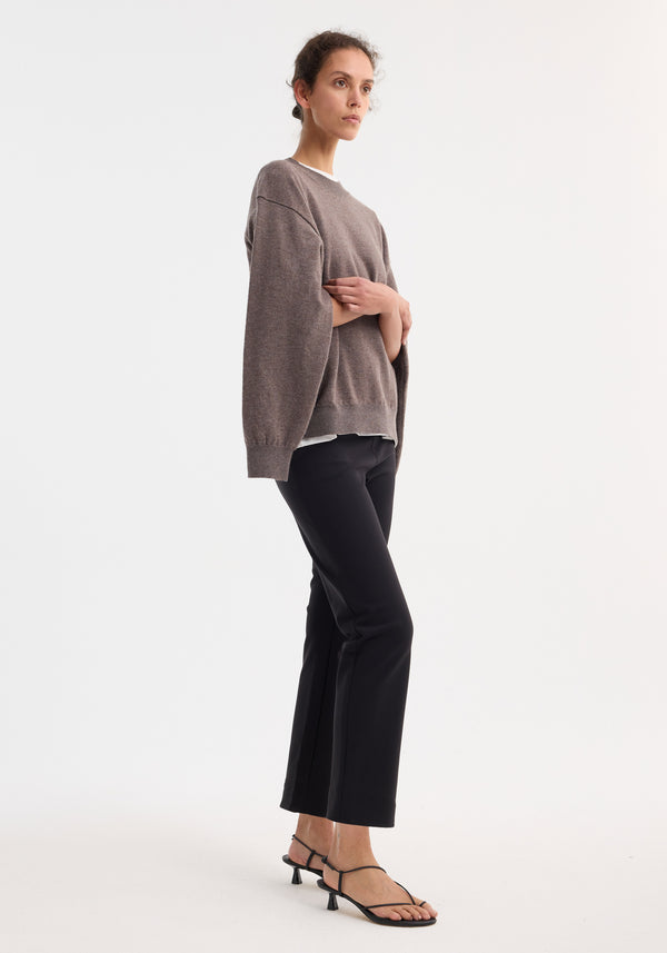 Model in profile wearing Cigarette scuba trousers | black, showcasing a tailored ankle-length silhouette and sleek cigarette leg design, paired with black strappy sandals.