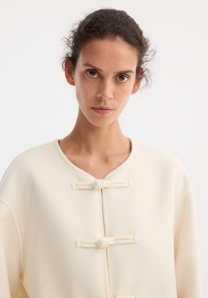 Young woman wearing the Mandarin double-faced wool jacket with pankou closures and embroidered edges, showcasing a collarless design and patch pockets.