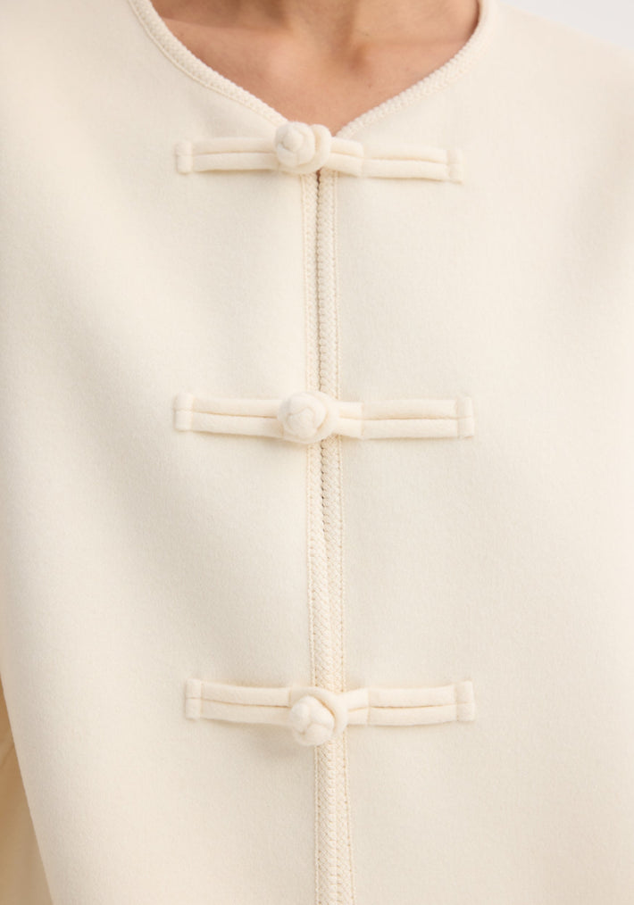 Mandarin double-faced wool jacket with pankou closures, embroidered edges, and patch pockets, showcasing a classic design with three knotted buttons down the front.