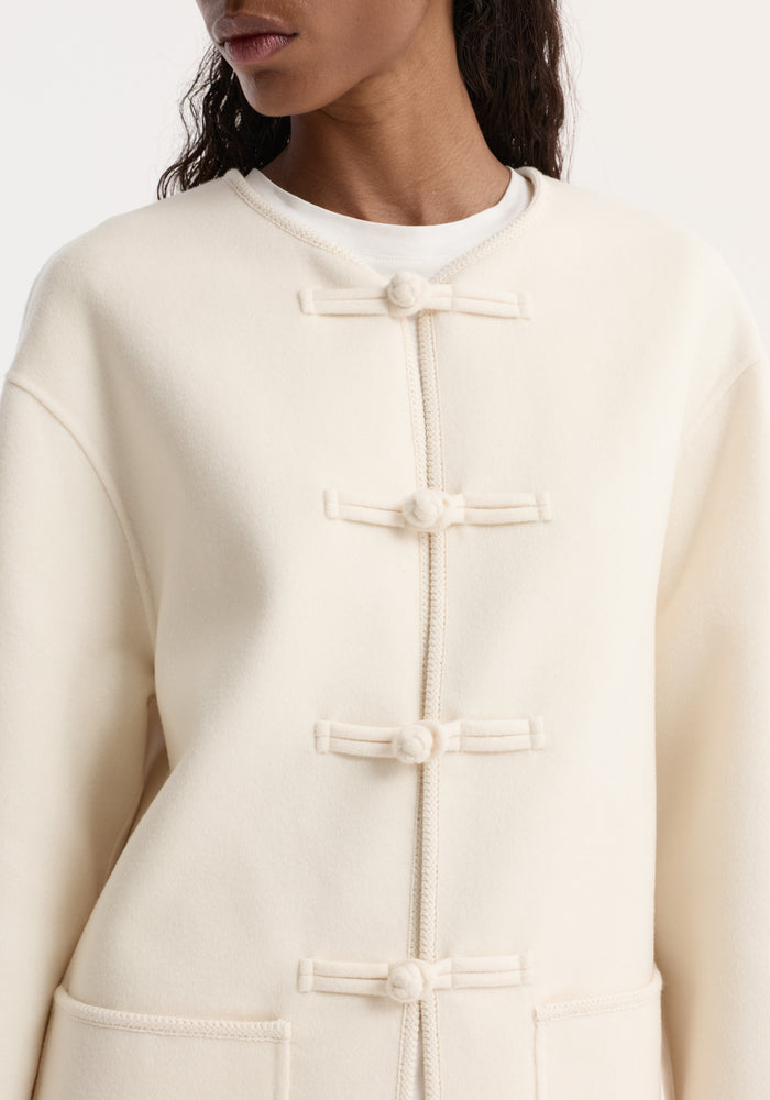 Double-faced wool pankou jacket with knot closures, embroidered edges, and patch pockets, worn over a white T-shirt.