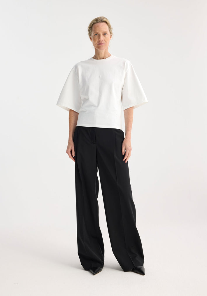 Model wearing the Fitted logo t-shirt in optic white, featuring a crew neck, tapered elbow-length sleeves, and subtle logo embroidery, paired with high-waisted black trousers.