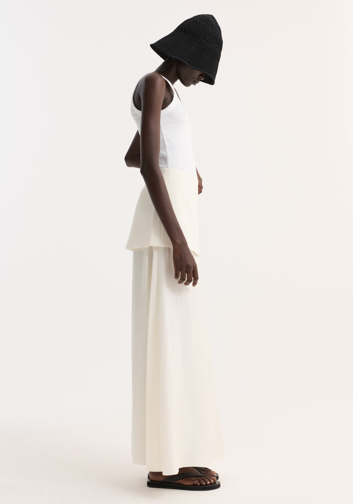 Model in an Integrated fluid silk skirt | cream, showcasing its high waist, layered panel detail, and flowing silhouette, paired with a white tank and black bucket hat.