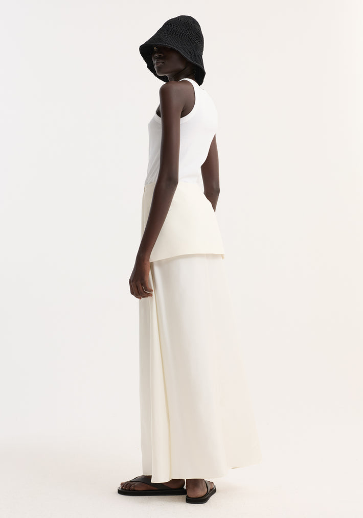 Model in profile wearing Integrated fluid silk skirt, cream; features a long, flowing design with high waist and subtle overlay, paired with minimalist accessories.
