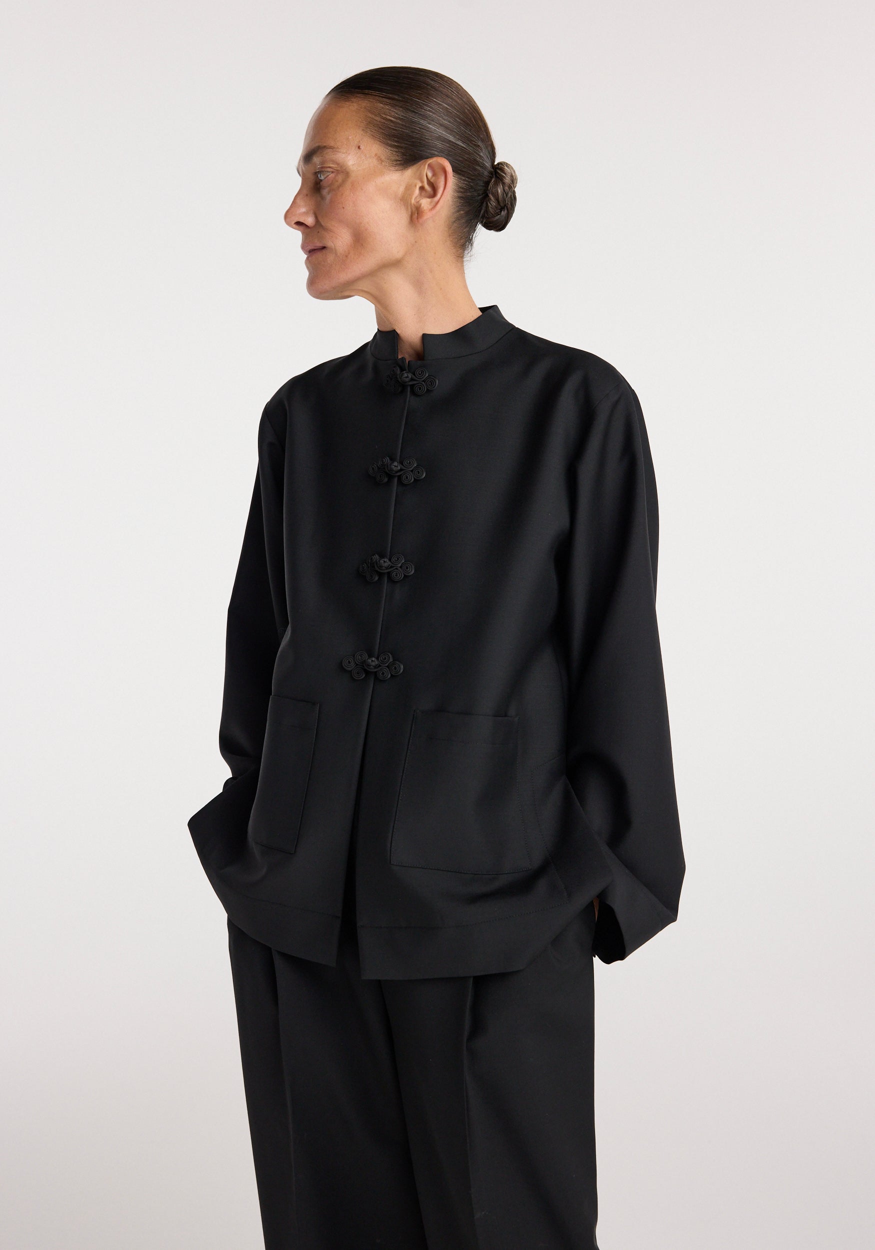 Woman wearing a black Pankou closure jacket | black with traditional knot buttons, large front pockets, and a mandarin collar, styled with matching black pants.