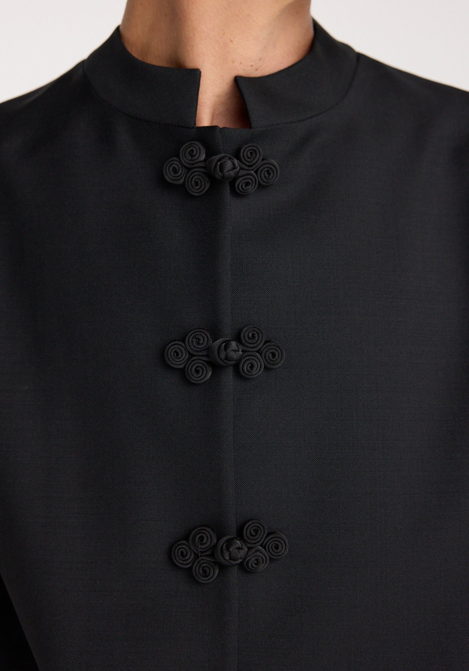 Close-up of a black Pankou closure jacket | black featuring three traditional Chinese-style knotted button fastenings on a high collar with minimalist design.