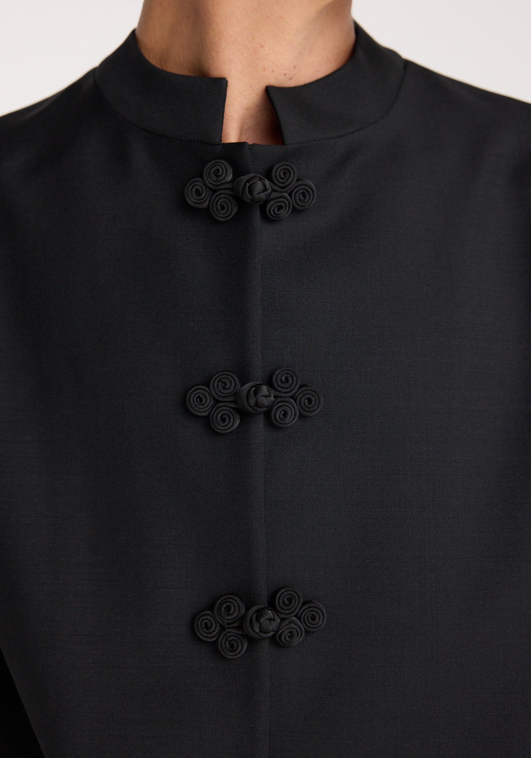 Close-up of a black Pankou closure jacket | black featuring three traditional Chinese-style knotted button fastenings on a high collar with minimalist design.