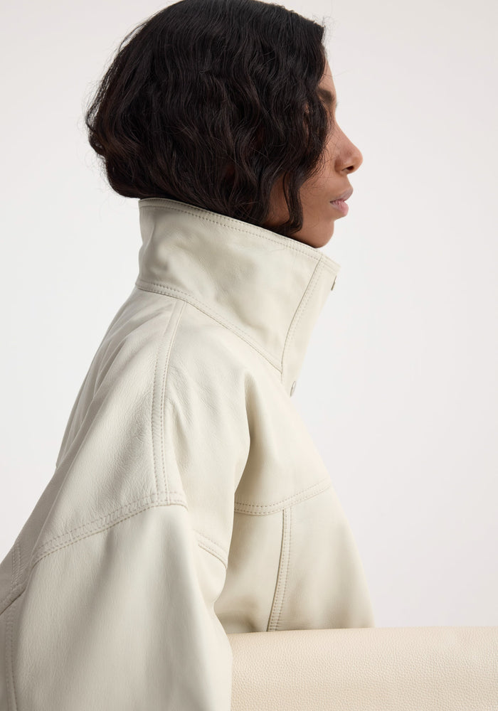 Side-profile of a person in a Reinvented leather jacket | chalk, showcasing its soft leather, high-collared bomber silhouette, and relaxed fit.
