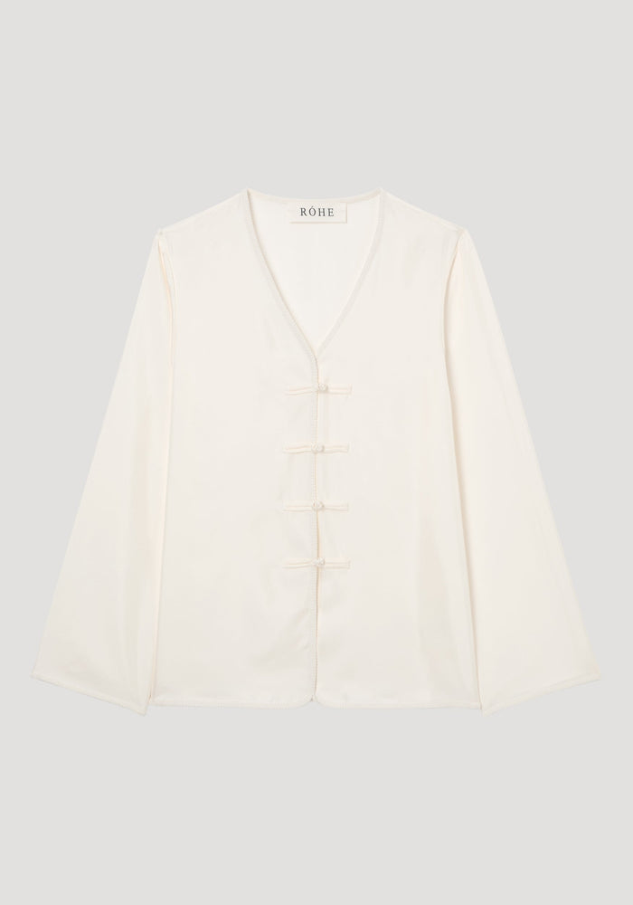 Mandarin silk top in ivory cream with V-neck, flared sleeves, pankou closures, and embroidered edges, laid flat on neutral background, showcasing a relaxed fit.