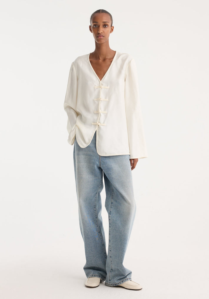 Model in Mandarin silk top with V-neck, pankou closures, and embroidered edges, paired with straight-leg jeans and slip-on shoes.