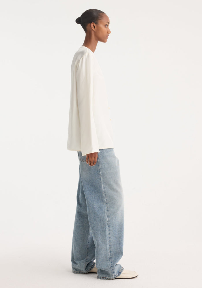 Side-profile of a model wearing a Mandarin silk top with pankou closures, embroidered edges, paired with high-waisted jeans and white loafers.