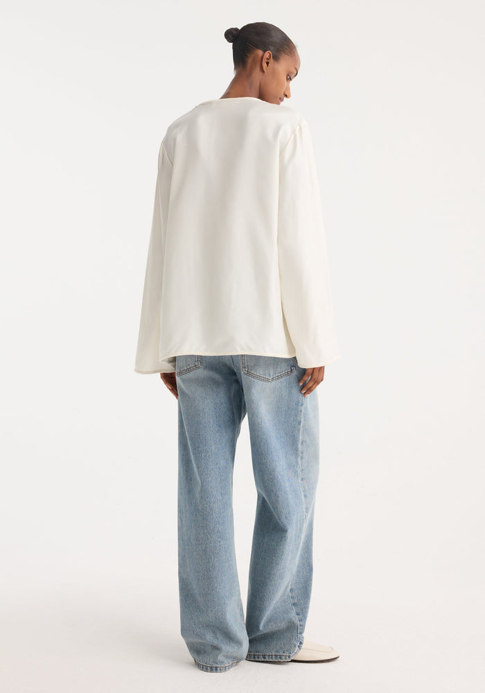 Person wearing a Mandarin silk top with pankou closures and embroidered edges, paired with wide-leg jeans, showcasing a relaxed and elegant style.