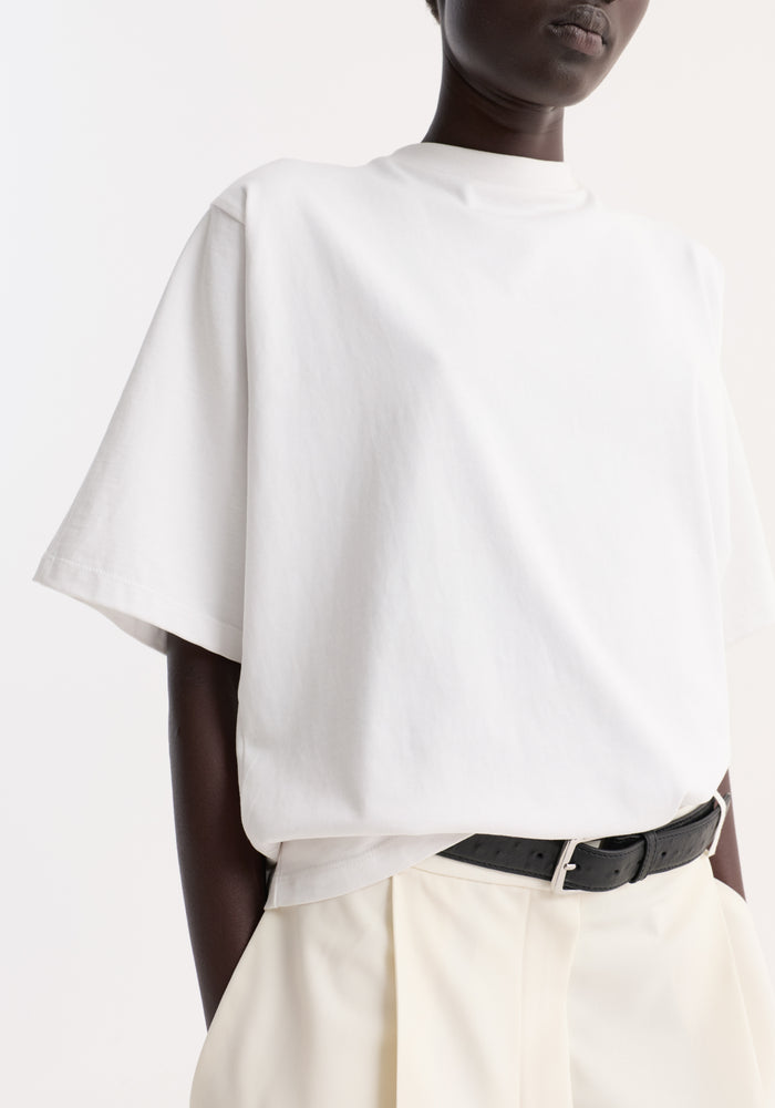 Model wearing Oversized cotton t-shirt with loose fit, crew neck, tucked into high-waisted trousers; features dropped shoulders and small logo on sleeve seam.