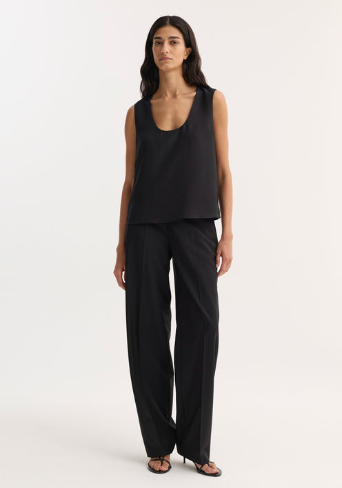 Model wearing a Scoop-neck silk top in black, featuring a deep scoop neckline and relaxed fit, paired with high-waisted trousers and heeled sandals.