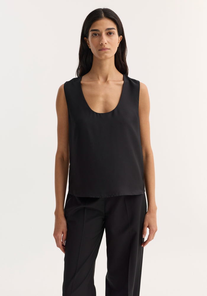 Model wearing a black scoop-neck silk top with a loose fit, showcasing minimalist style and ideal for layering.