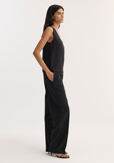 Model wearing a Scoop-neck silk top in black, featuring a deep scoop neckline and relaxed fit, paired with high-waisted trousers and heeled sandals.