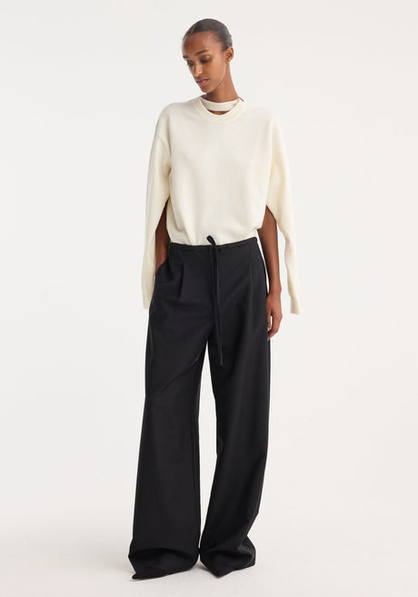 Model wearing Relaxed drawstring trousers in black, featuring a wide-leg silhouette, drawstring waistband, front pleats, and back welt pockets, paired with an ivory sweater.