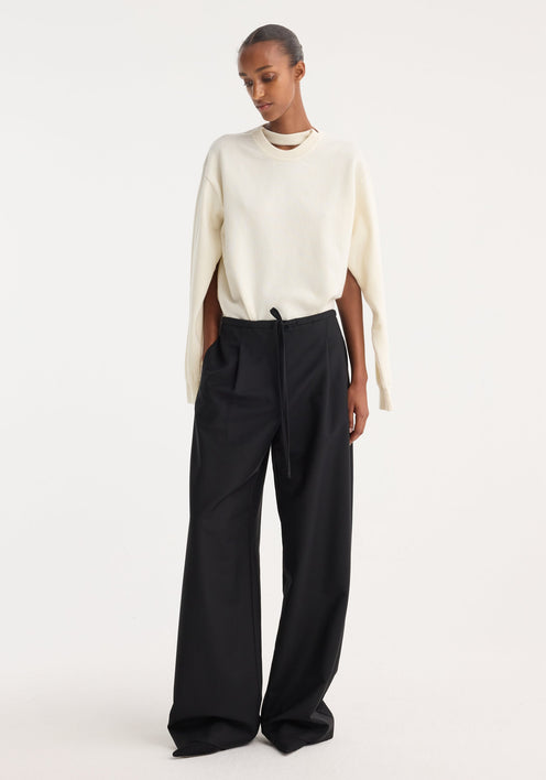 Model wearing Relaxed drawstring trousers in black, featuring a wide-leg silhouette, drawstring waistband, front pleats, and back welt pockets, paired with an ivory sweater.