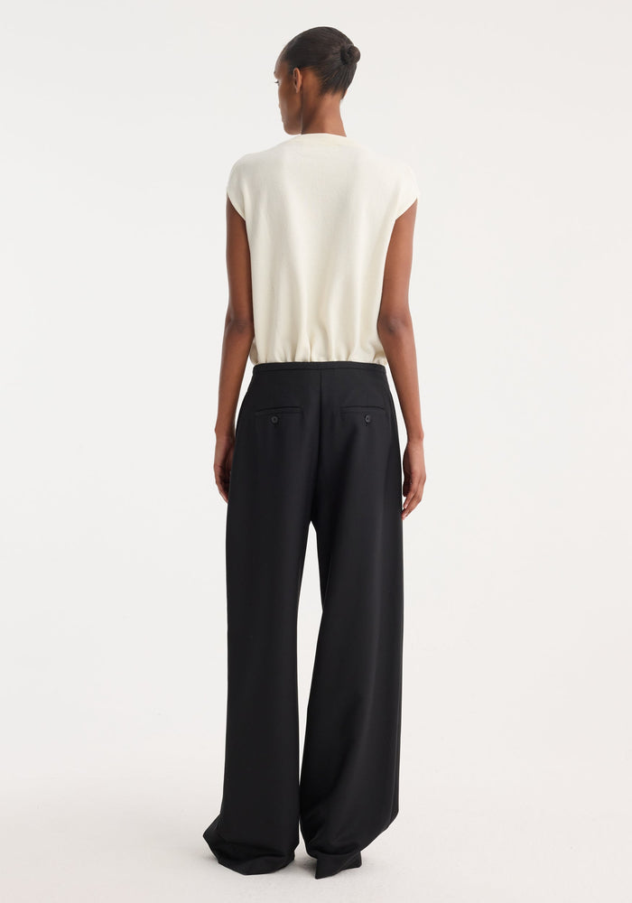 A woman wears Relaxed drawstring trousers | black, featuring a wide leg, drawstring waistband, and back welt pockets, paired with a sleeveless top.