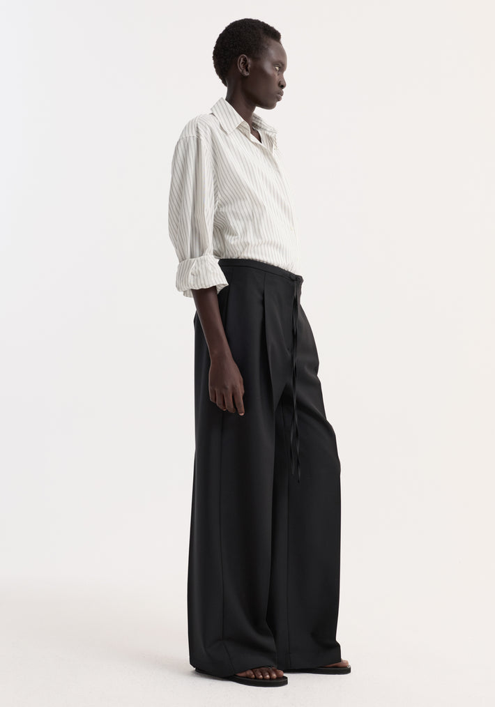 Profile view of a person wearing Relaxed drawstring trousers in black, featuring a long, wide-leg design with a drawstring waistband, styled with a button-up shirt.