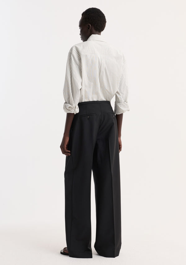 Back view of a person wearing black Relaxed drawstring trousers with a wide-leg design, front pleats, and a drawstring waistband, styled with a tucked-in striped shirt.