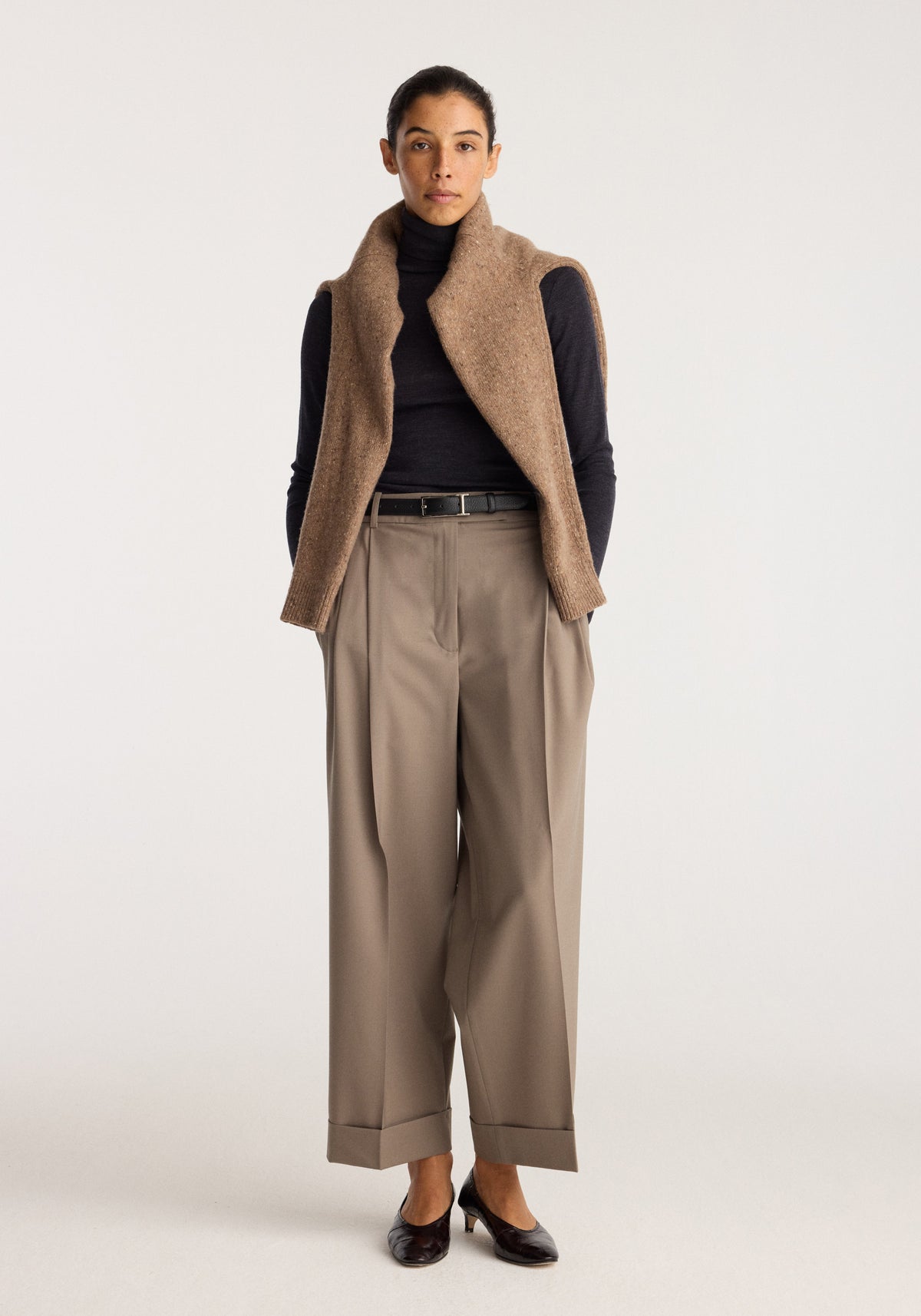 High-waist turn-up trousers | taupe worn by a model with a black top, brown vest, belt and black shoes, showing the wide-leg fit and cuffed hems