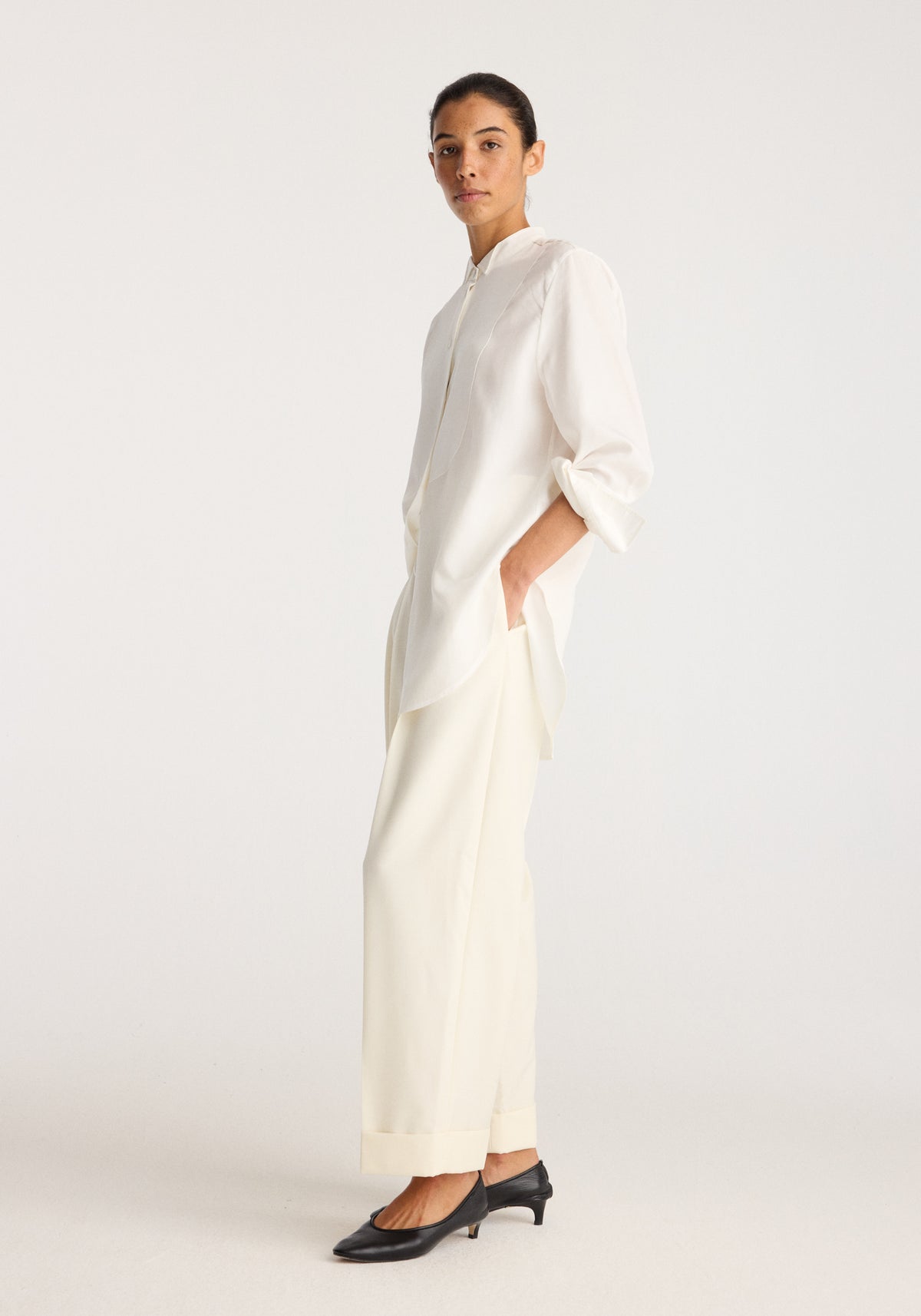 High-waist turn up trousers | off white shown on a model with turned-up hems styled with a white blouse and black pointed heels in a minimal studio setting