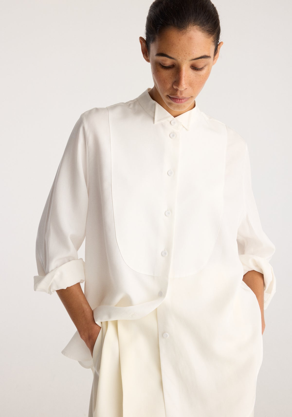 High-waist turn up trousers | off white worn by a model with a white button-up shirt and hands in pockets