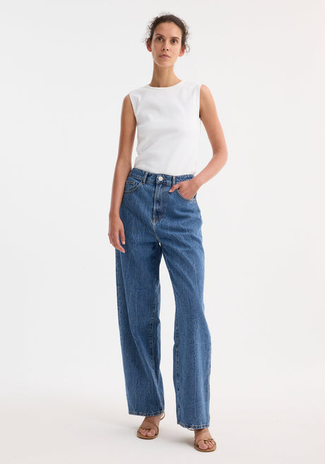 Signature baggy fit denim in mid denim blue, featuring a low-waist, wide-leg style. Model wears jeans with a sleeveless top and strappy sandals.