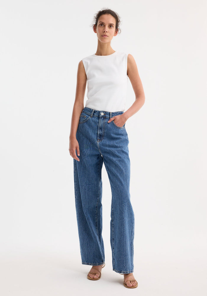 Signature baggy fit denim in mid denim blue, featuring a low-waist, wide-leg style. Model wears jeans with a sleeveless top and strappy sandals.