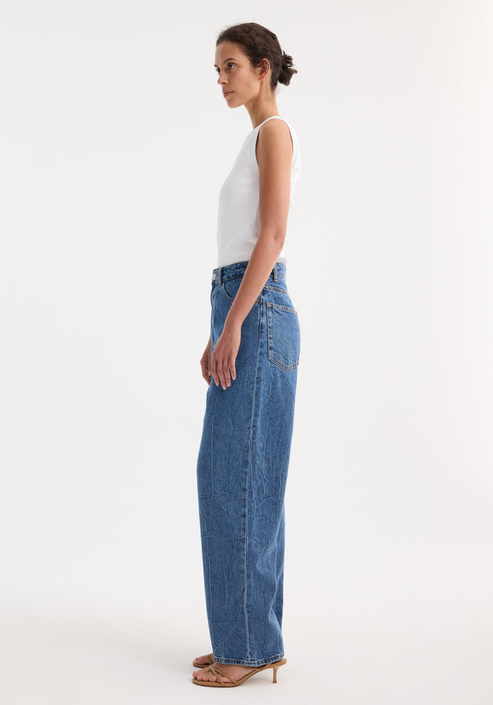 Signature baggy fit denim in mid denim blue, featuring a low-waist, wide-leg style. Model wears jeans with a sleeveless top and strappy sandals.