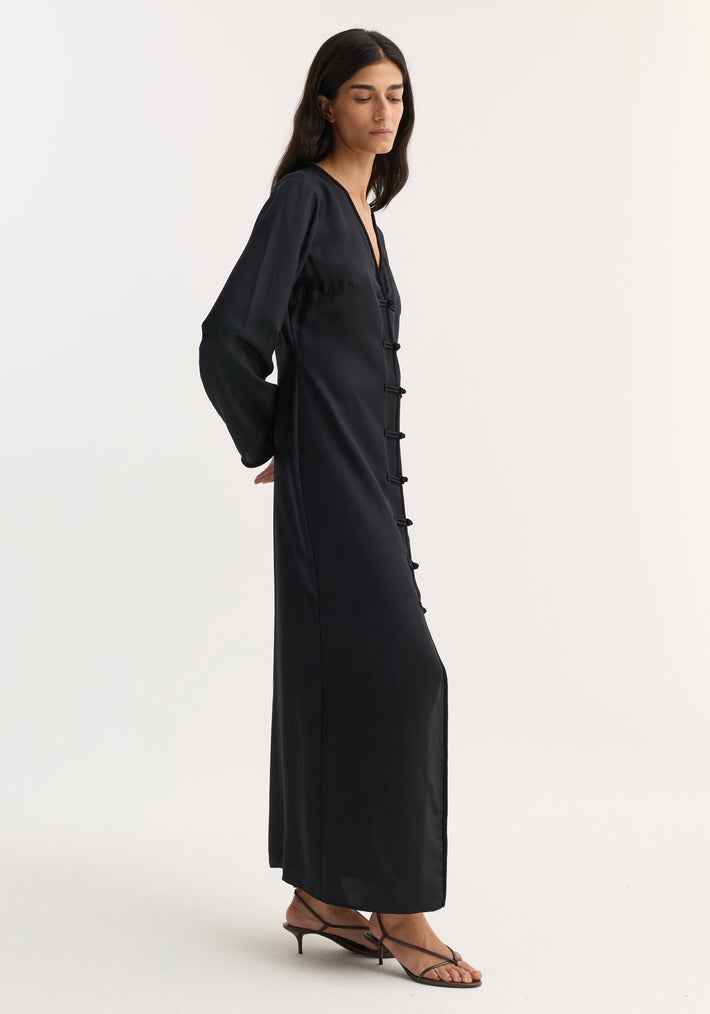 Model in Mandarin silk dress | black, featuring a V-neck, long sleeves, pankou closures, and a high front split, paired with brown strappy kitten heel sandals.