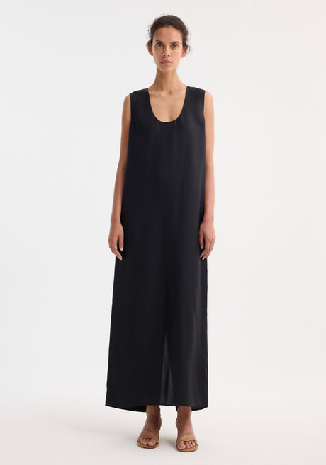 Model in a Scoop-neck silk dress | black, floor-length, sleeveless, with a relaxed silhouette and subtle front slit, paired with tan strappy sandals.