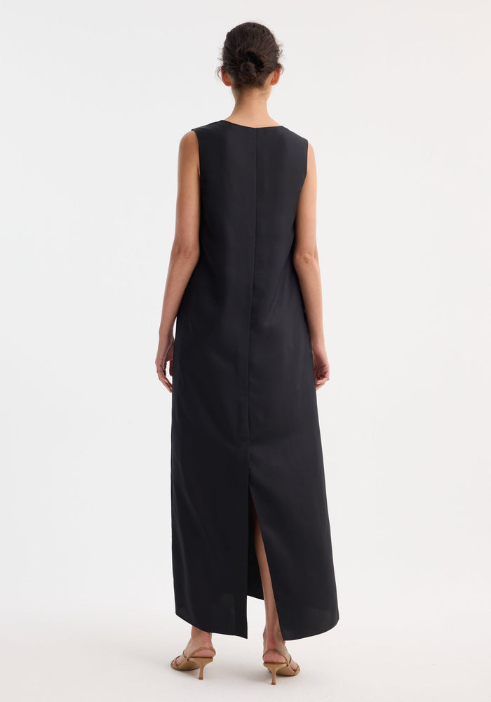 Woman in a sleeveless, ankle-length Scoop-neck silk dress | black, with a back slit, low bun hairstyle, and tan heeled sandals, showcasing elegance and comfort.