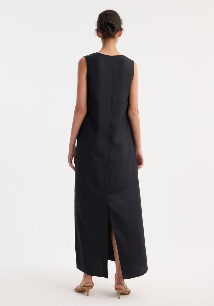 Woman in a sleeveless, ankle-length Scoop-neck silk dress | black, with a back slit, low bun hairstyle, and tan heeled sandals, showcasing elegance and comfort.