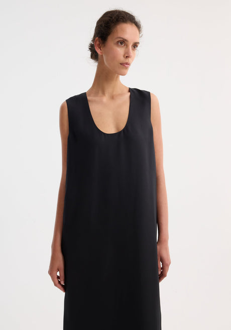 Model in a Scoop-neck silk dress | black, floor-length, sleeveless, with a relaxed silhouette and subtle front slit, paired with tan strappy sandals.
