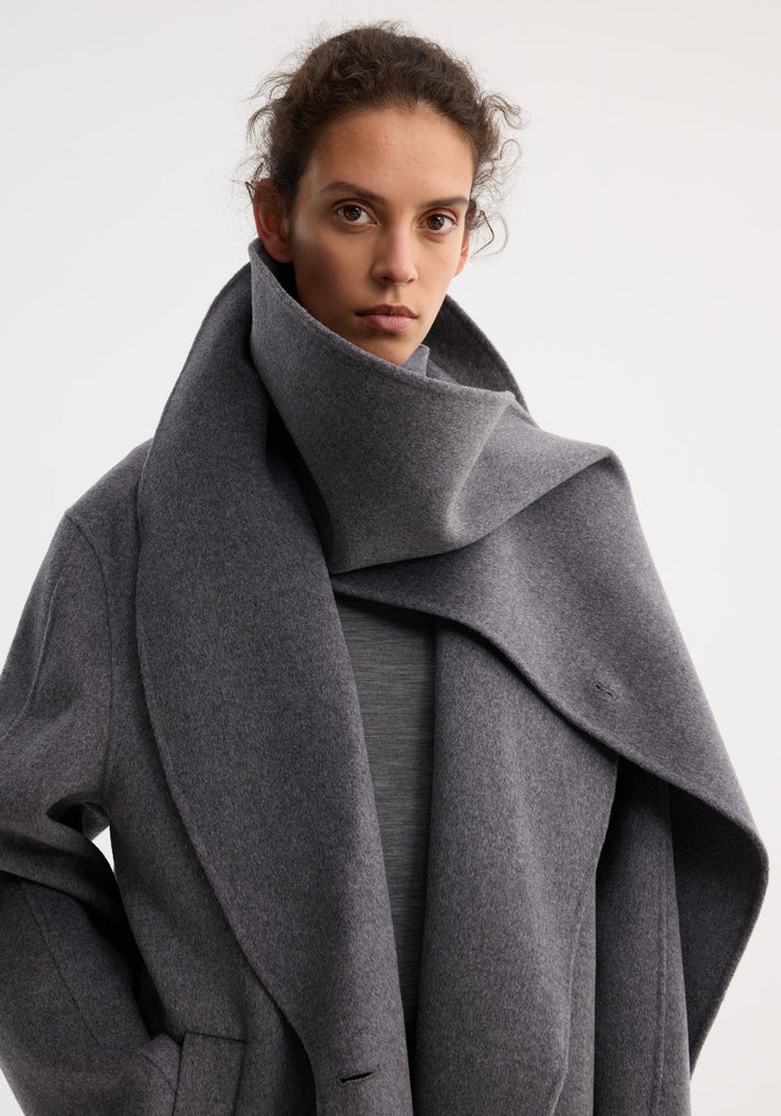 Signature double-faced scarf coat in mid grey melange, featuring a sculptural double-layered scarf collar and broad lapels, worn by a young adult against a light background.