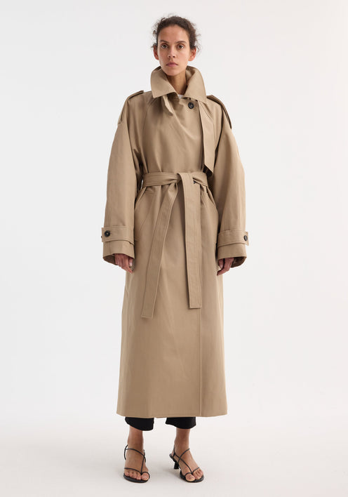 Model in Oversized classic trench | clay, featuring double-breasted design, epaulettes, belted waist, and side pockets, over black cropped trousers and strappy sandals.