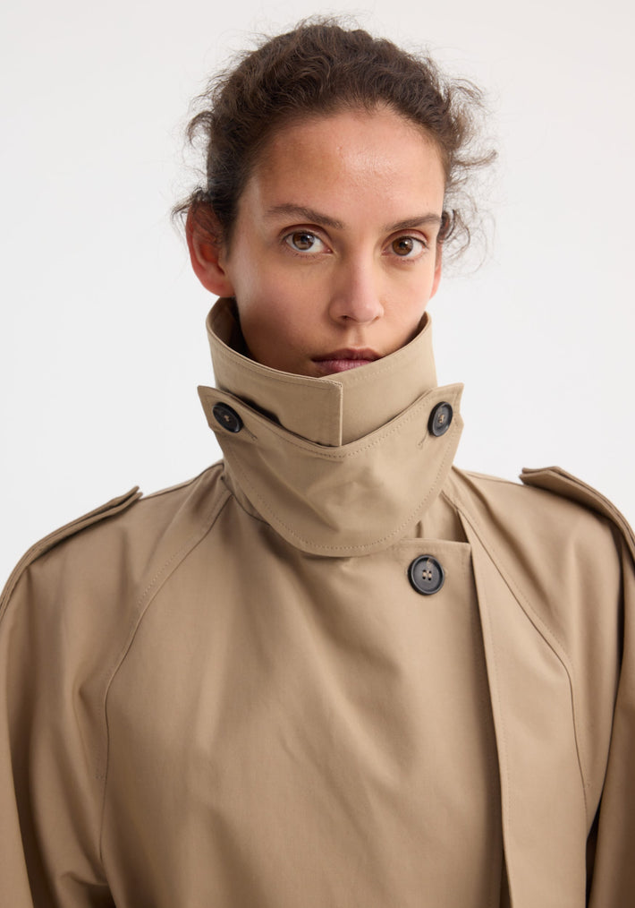 Model wearing oversized classic trench | clay with dark buttons, shoulder epaulettes, wrap belt, and side pockets, crafted from high-quality cotton.