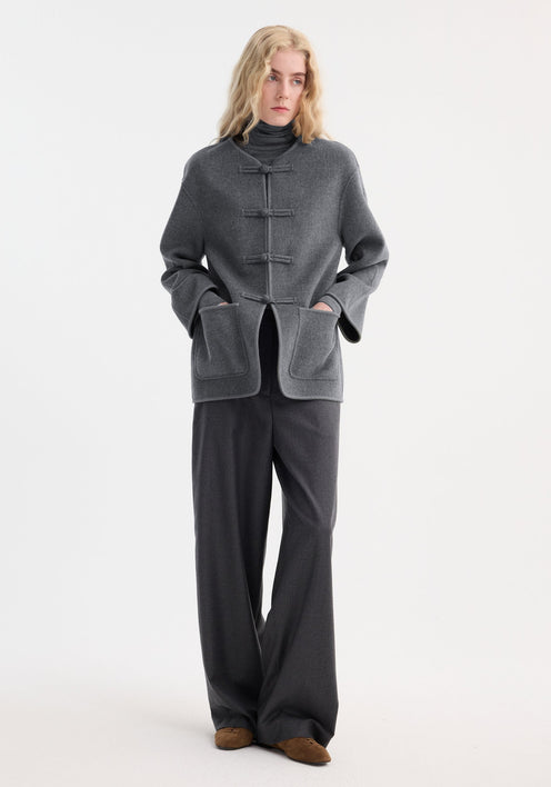 Model in a minimalist grey ensemble featuring the Róhe 'Marie' mandarin double-faced wool jacket with pankou closure, embroidered edges, and patch pockets.